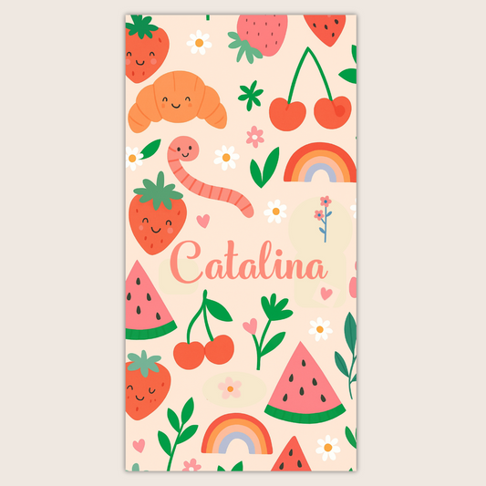Toalla personalizada con fresas, cerezas, arcoíris y nombre en el centro sobre fondo crema.